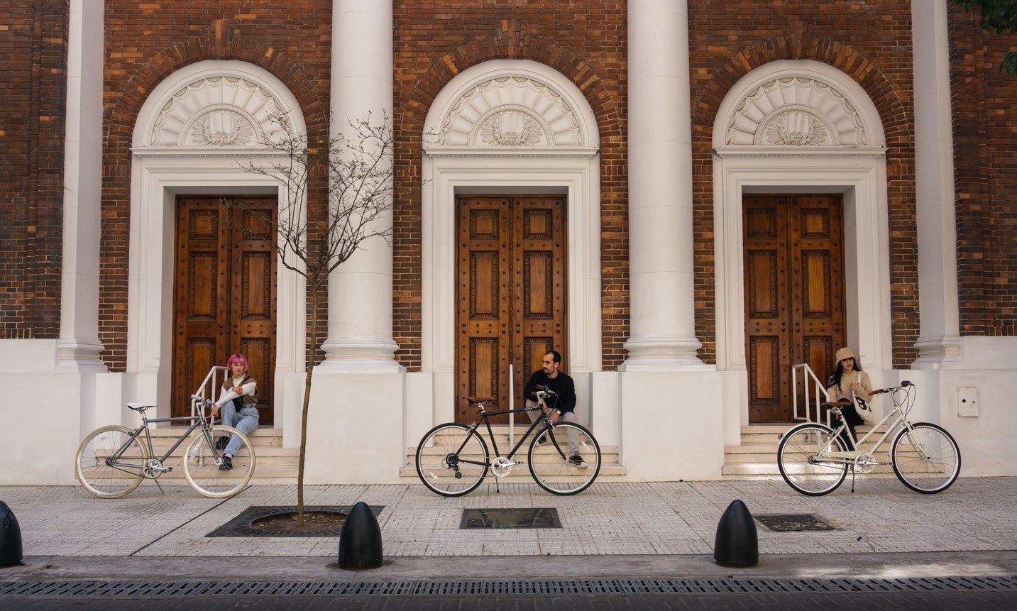Three people with their bicycles in front of large wooden doors
