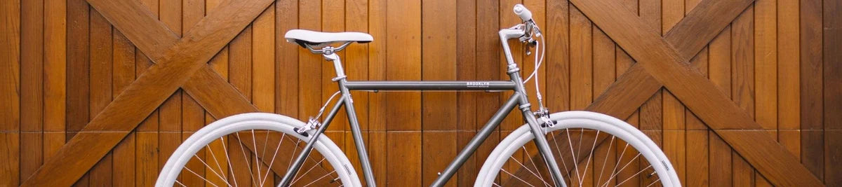 Silver single speed bike with white tires against vertical wooden panel background