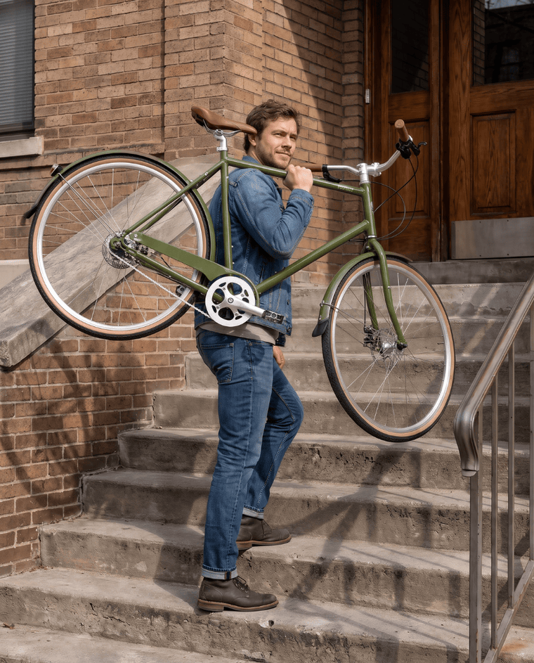 A rider carrying an internally geared Army Green Driggs 8 up the front steps of a Brooklyn brownstone