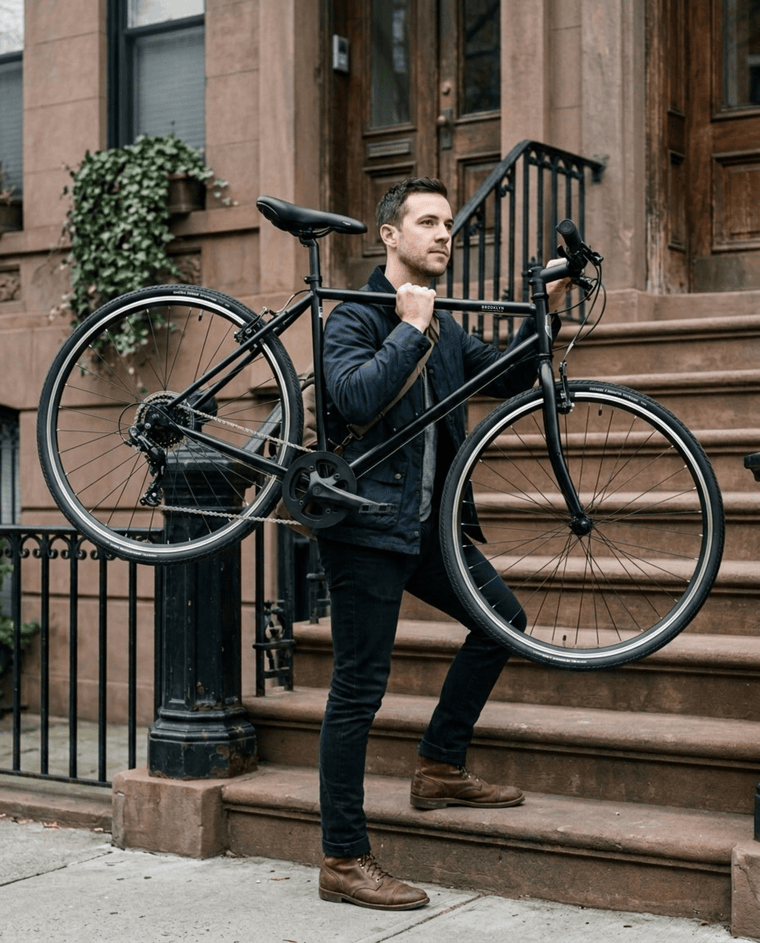 A rider carrying a matte black Roebling up the front steps of a Brooklyn brownstone